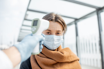 Measuring temperature with infrared thermometer of a young woman in face mask at a checkpoint...