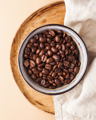 Arabica coffee beans in a ceramic bowl on a wooden tray on a brown background. 