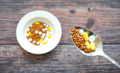 Buckwheat in a spoon mixed with tablets on the background of a plate