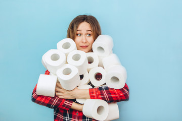 Girl with a lot of rolls of toilet paper in her hands on a blue background. Lack of toilet paper...