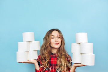 Girl with a lot of rolls of toilet paper in her hands on a blue background. Lack of toilet paper during the coronavirus pandemic. Lack of hygiene products.