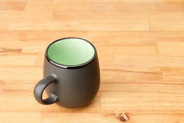 A dark mug stands on a wooden tabletop.
