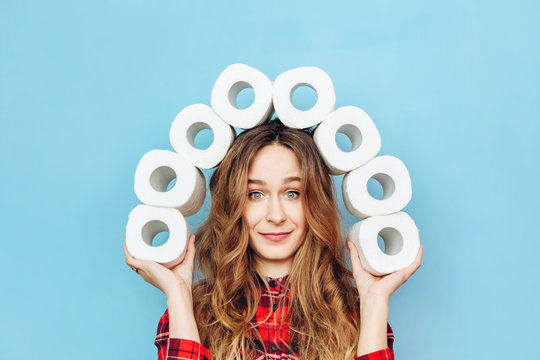Girl with a lot of rolls of toilet paper in her hands on a blue background. Lack of toilet paper during the coronavirus pandemic. Lack of hygiene products.
