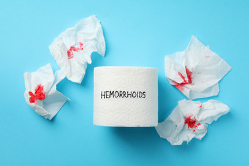 Toilet paper with Hemorrhoids and paper with blood on blue background, top view