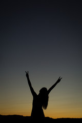 Fototapeta na wymiar high school senior girl silhouette showing peace signs with hands in front of sunset