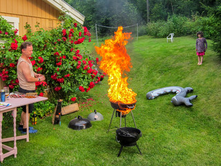 Family, father and child having a outdoor garden barbecue grill party in the backyard. Fail with grill on fire, inferno with big flames. - obrazy, fototapety, plakaty
