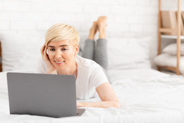 Happy mature woman laying in bed and watching movie