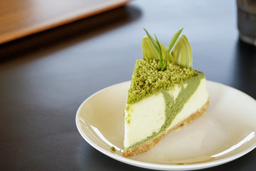 Sweet or dessert, a matcha green tea cheesecake topping with crush chocolate and decor with tea leaf on white plate on black table with a cafe environment