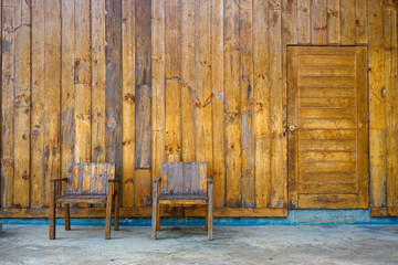 Background, Two chairs place in front of the wall on a concrete floor and there's a door on the right-hand side. those of all made from wood