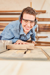 Carpenter apprentice saws wood on the circular saw
