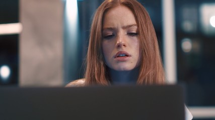 Close up of beautiful serious redhair woman freelancer works in home typing email on laptop focused girl use computer for study online sitting on couch female user busy internet job social