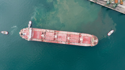 Aerial top down view of Tug boats assisting big cargo ship. Large cargo ship enters the port...