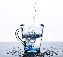 A stream of water pours into a glass Cup on a white background.
