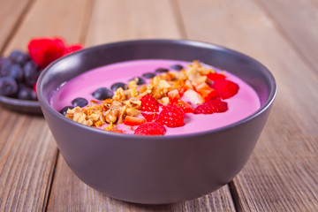 Smoothie bowl with berries and muesli on the wooden table.