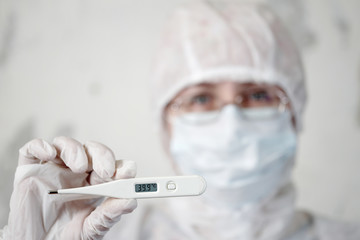 female doctor in medical mask on face holds thermometer with hand