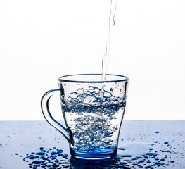 A stream of water pours into a glass Cup on a white background.