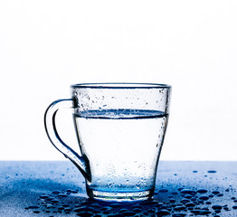 Clear, transparent water in a glass Cup on the table on a white background. Drops of water on the table next to it.