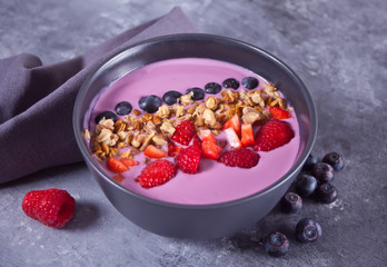 Smoothie bowl with berries and muesli on the gray table.