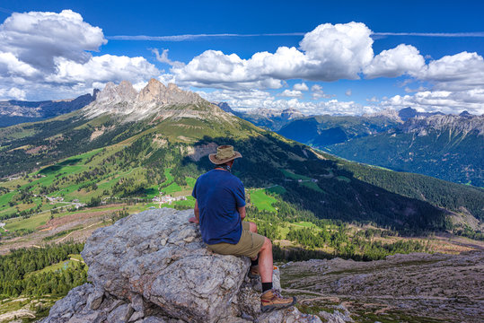 Hiker sitting at summit of Pulpito di Cima Pope looking at Rosengarten mountains, South Tyrol, Italy