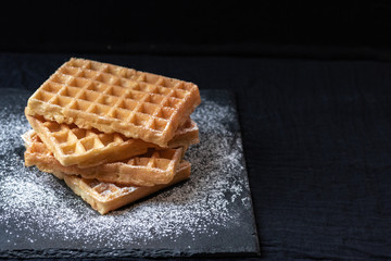 Sweet tasty Belgian waffles close-up, sprinkled with powdered sugar