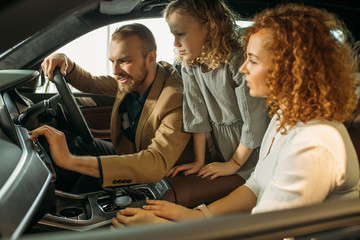 happy caucasian family in dealership. young family came to get new automobile in cars shop. they discuss, choose and buy new perfect fast car