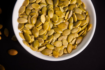 Pumpkin seeds in a white bowl on the black background.