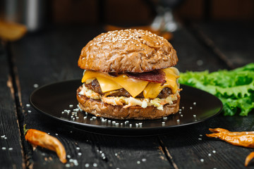 Appetizing bacon burger on a black plate on the dark wooden table, side view, horizontal