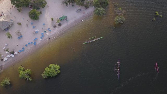 Aerial drone view of Hawaiian canoes arriving at Alter do Chao city beach on the Tapajos River in the Amazon rainforest. concept of sport, healthy life, travel, holidays, tourism and leisure.4K