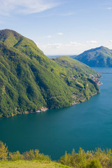 A top view of Lake Lugano, Switzerland from the height of Mount Monte Bre. Beautiful mountain scenery on a sunny summer day. View of Lake Lugano and the Alpine mountains covered with green plants.