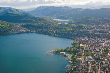 Fototapeta na wymiar Top view of the city of Lugano, Switzerland from the height of Mount Monte Bre. Beautiful mountain scenery on a sunny summer day. View of Lake Lugano and the Alpine mountains.