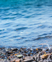 Beautiful black-toned rocks are rounded, curved along the beach, where the seawater is periodically affecting the shore. There is a background sky. In the evening there was a soft light of the sun.