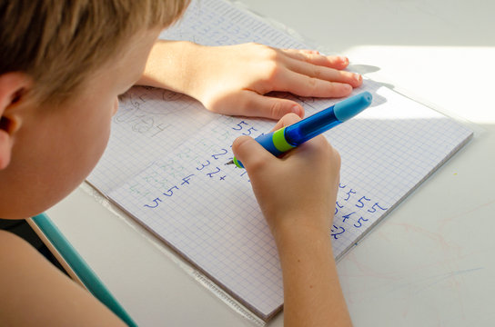 Kid Hands Doing Math Homework. Close Up Of Young Boy Hand Holding Pen And Writing A Math Homework Close-up. Concept Of Education At Home.