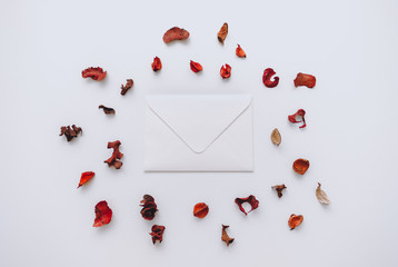 White blank paper envelope on a white background around decorated with dried petals. Top view