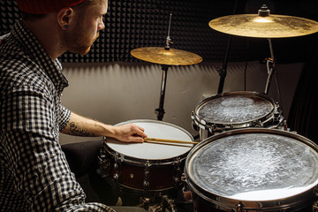 young caucasian drummer rehearsing on drums before rock concert. professional artiste man recording music on drum set in dark studio