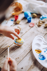 Happy easter! Cute little child girl painting with blue and yellow colors Easter eggs. family preparing for Easter. Hands of a girl with a easter egg. close-up