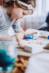 Happy easter! Cute little child girl painting with blue and yellow colors Easter eggs. family preparing for Easter