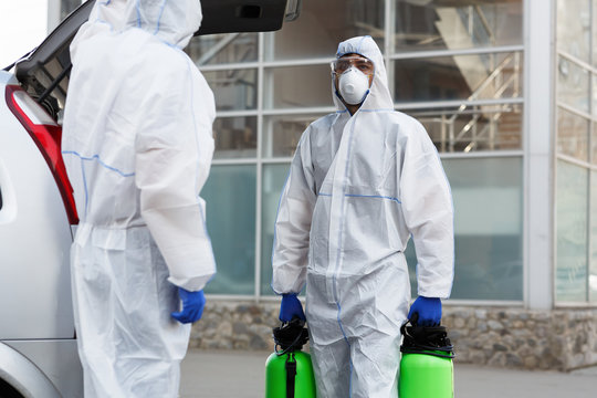 Man in coronavirus suit holding spray bottles with disinfecting chemicals