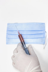 Doctor holding medical syringe with blood and a medical mask on a white background