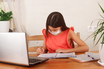 Child girl in medical mask on her face doing homework on distance education. Homeschooling, E-learning and self-isolation at home during quarantine concept