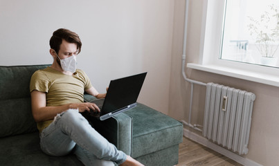 man in a medical mask works with a laptop at home, quarantine self-isolation.