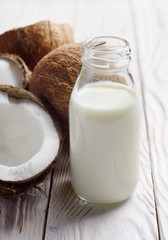 Fototapeta na wymiar Glass bottle with milk or yogurt on white wooden kitchen table with coconut aside