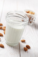 Milk or yogurt in mason jar on white wooden table with almonds in airtight conainer aside
