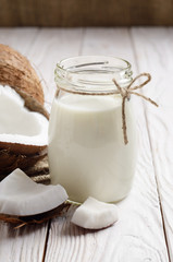 Glass bottle with milk or yogurt on white wooden kitchen table with coconut aside