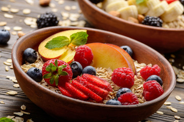 Fruit healthy muesli with peaches strawberry almonds and blackberry in clay dish on wooden kitchen table