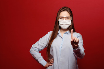coronavirus pandemic, close-up portrait of young woman on red background in protective medical mask,