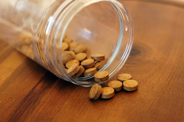 A jar with brown natural pills lying on a wooden table