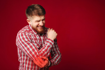 Bearded man having elbow pain on red background. Man suffering from arm injury.