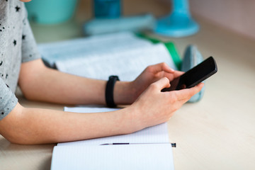 Close up of young school girl working at home with class notes checking mobile phone and studying. Distance education and learning concept during quarantine