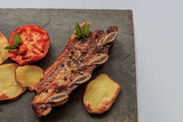 Grilled steak detail with legs and tomato on stone plate with white table. American food concept