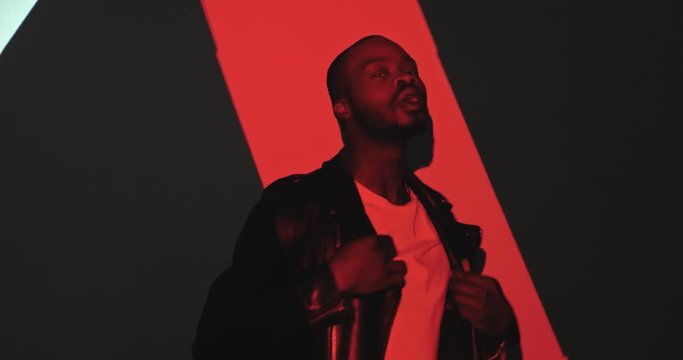 Portrait of African American young handsome stylish man in moving like dancing and posing to camera in black, blue and red projection in patterns and curves. Projected lines colors and graphic on male